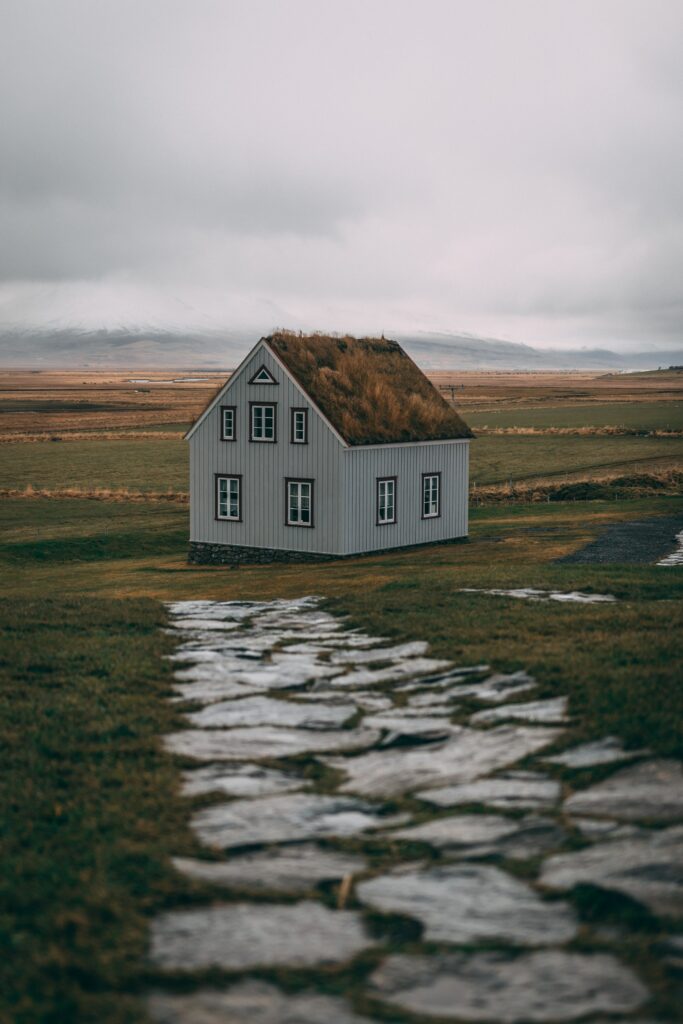 Quaint house with green grass roof in open field with stone path under cloudy sky rural charm Wallpaper