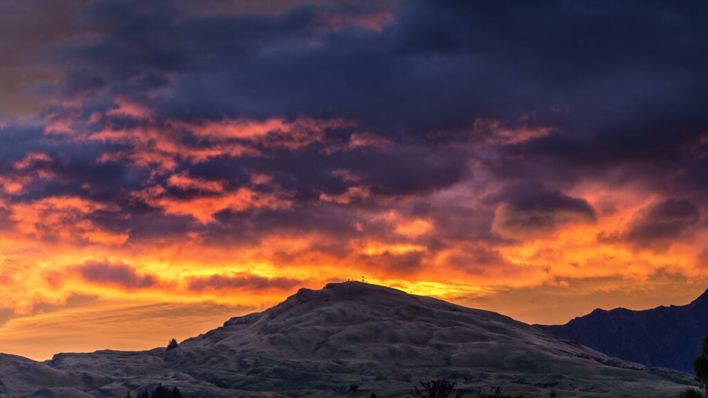 Dramatic Queenstown New Zealand sunset over rolling mountains vibrant orange yellow clouds Wallpaper
