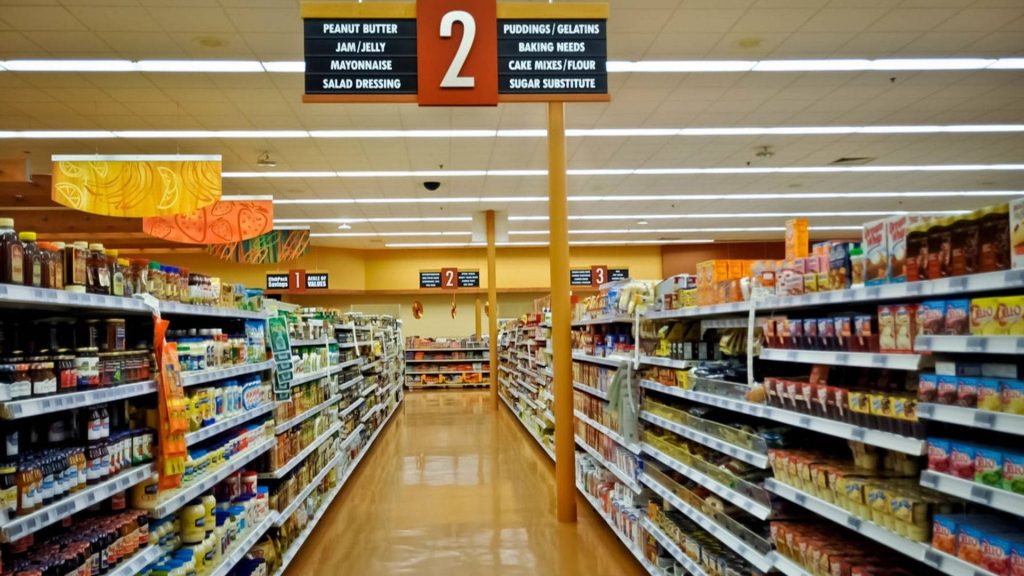 Quiet grocery store aisle with bright lights glossy yellow floor and stocked pantry shelves Wallpaper