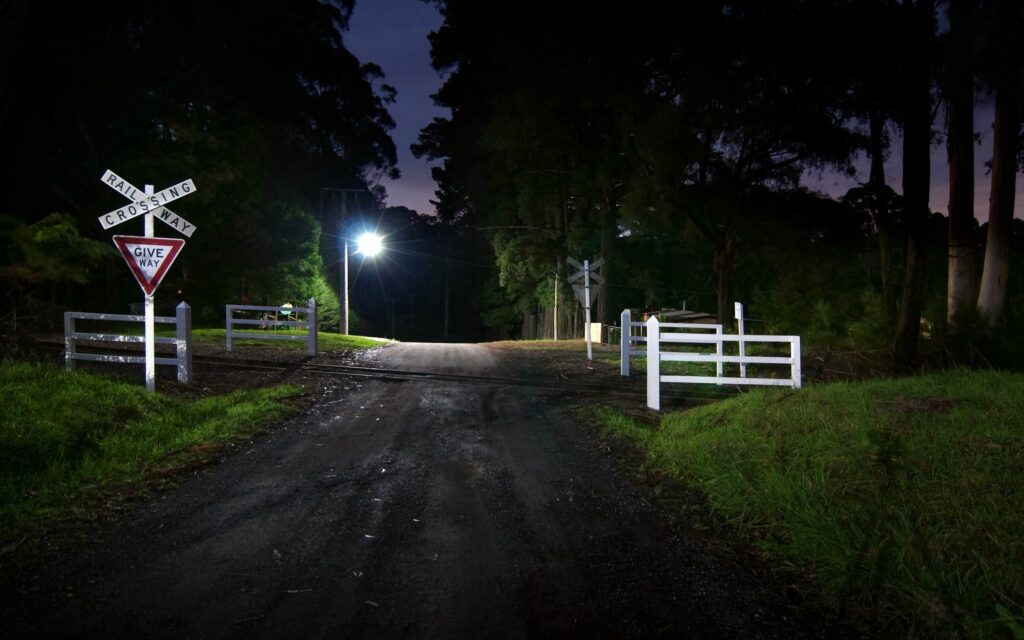 Night rural road with streetlight white fences railway crossing and give way signs peaceful scene Wallpaper