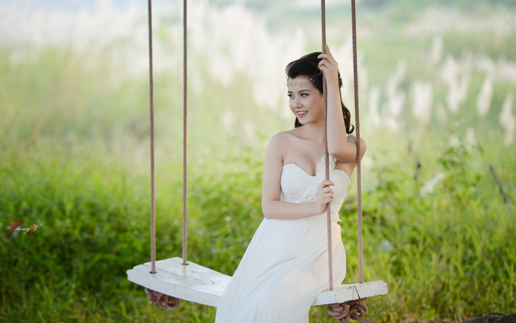 Radiant bride in elegant white dress on rustic swing surrounded by lush greenery and sunlight Wallpaper