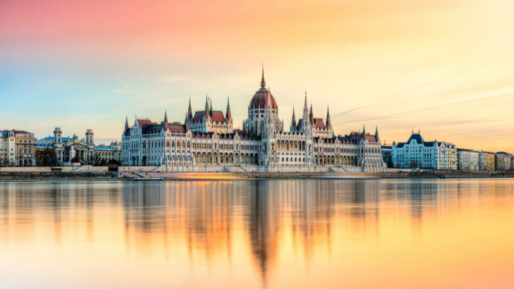 Budapest Parliament Building reflecting on calm Danube River under pastel sky wallpaper background