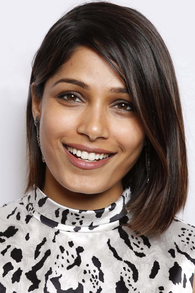 Close-up portrait of actress Freida Pinto smiling in black and white abstract high-neck garment Wallpaper