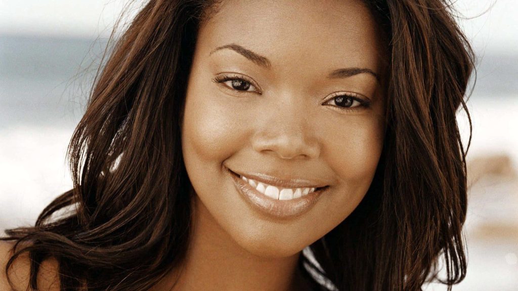 Radiant close-up of Gabrielle Union smiling with soft natural light and serene beach background Wallpaper