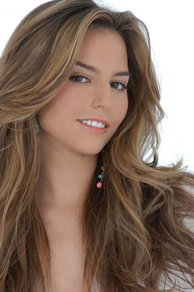 Radiant portrait of Genesis Rodriguez smiling with voluminous brunette hair and blonde highlights Wallpaper