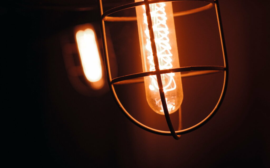 Glowing Night: Mesmerizing Edison Lamp Illuminates the Darkness on a Striking Black Canvas Wallpaper