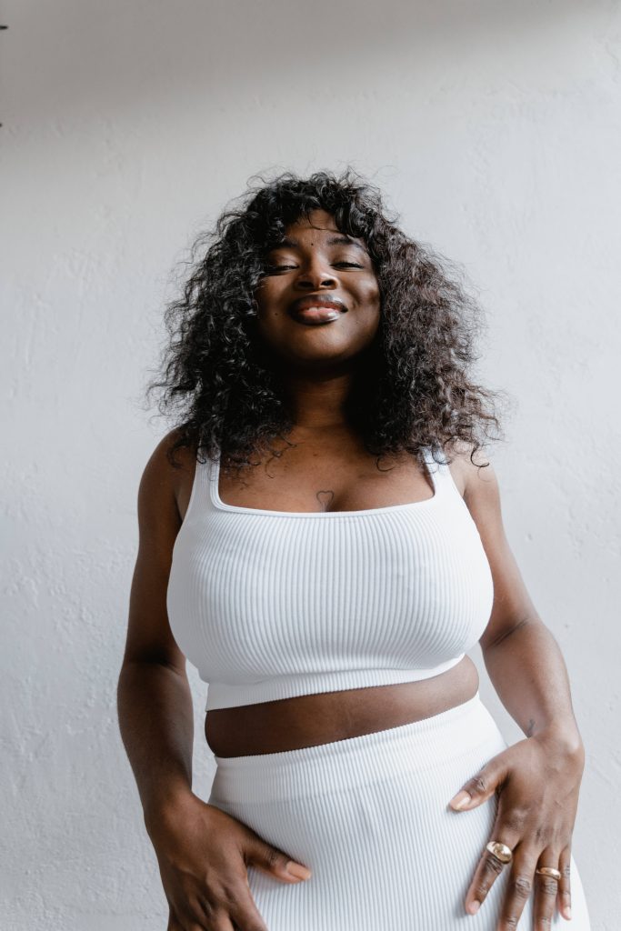 Plus-size woman in white ribbed outfit smiling confidently bright minimalist wallpaper background