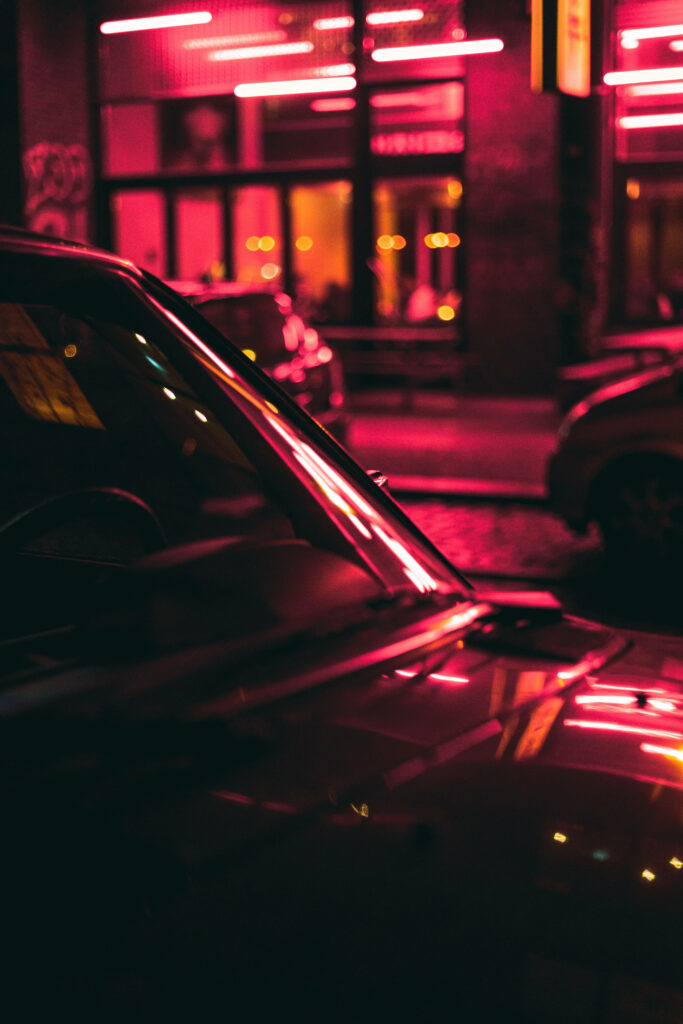Vibrant Glow: Dramatic Red Neon Lights Cast a Haunting Reflection on Nearby Parked Car Wallpaper
