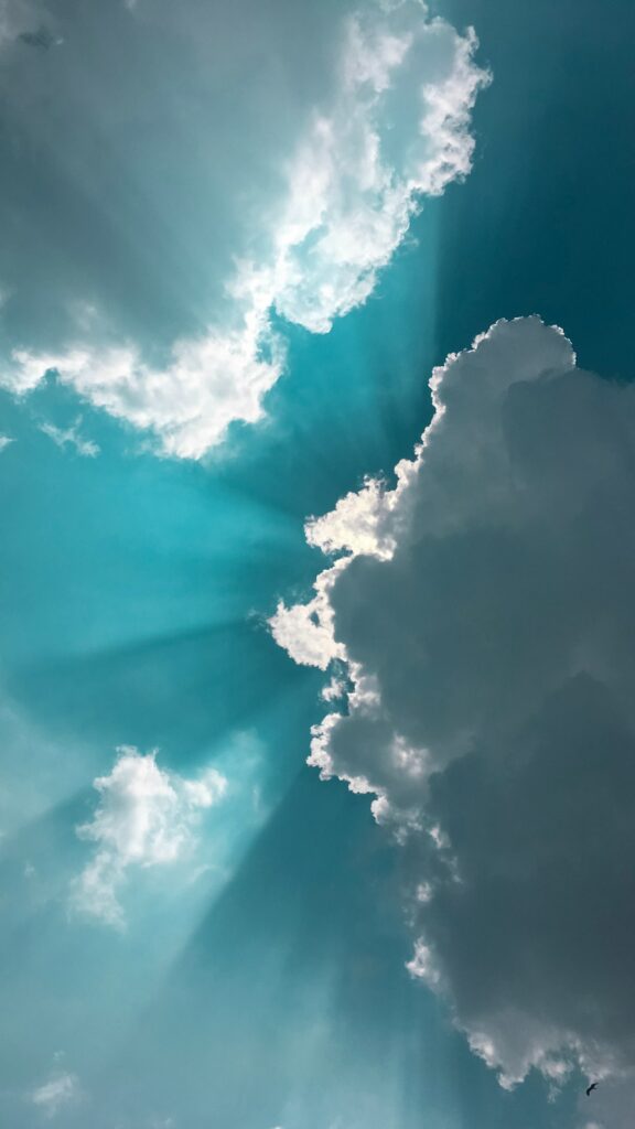 Soft white clouds with radiant sun rays shining through against a vibrant blue sky background Wallpaper