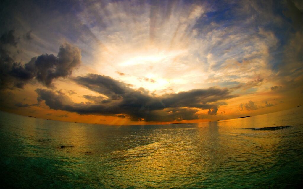 Sunrise over tranquil sea with dramatic clouds and vibrant colorful panoramic sky wallpaper background