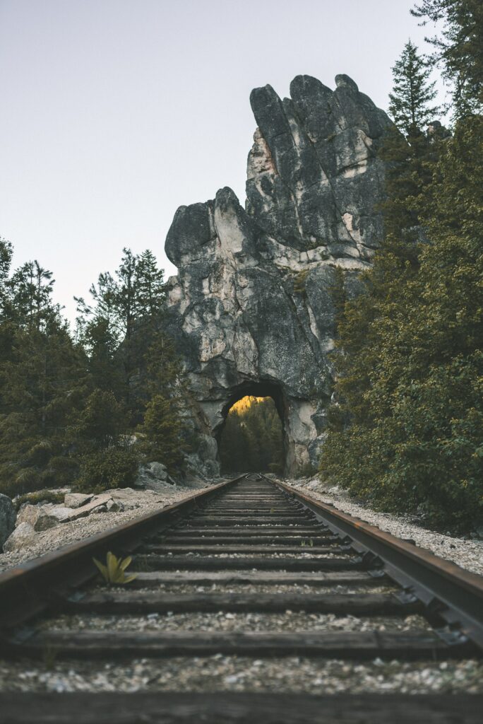 Railway tracks pass through a stone arch in rugged rock surrounded by dense green forest wallpaper