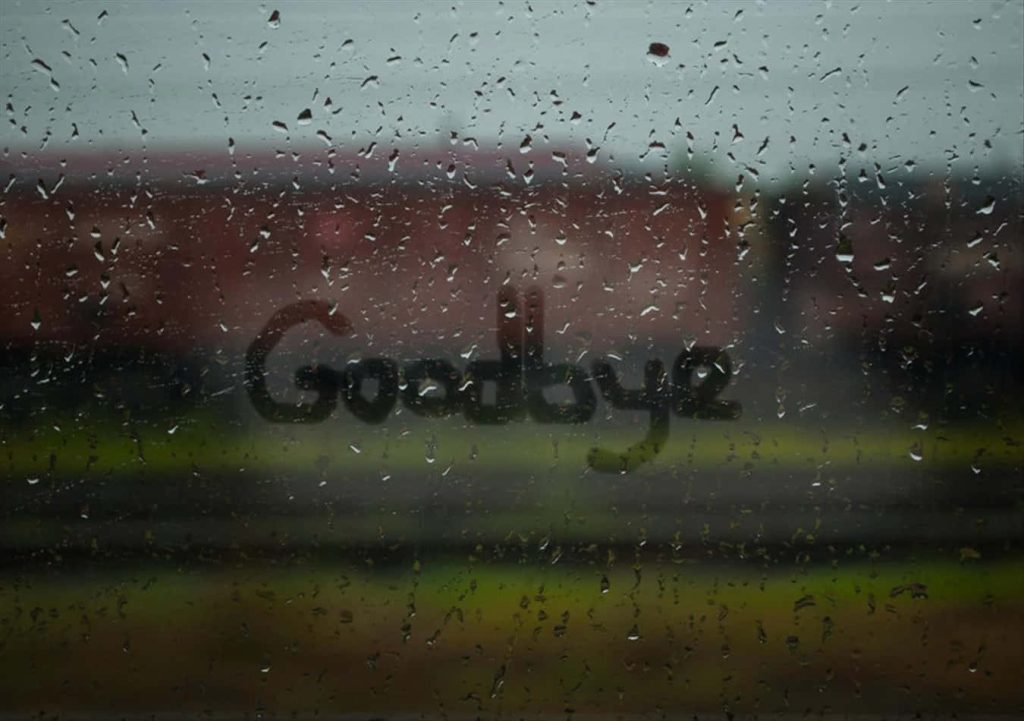 Rainy window with Goodbye message on glass and blurred moody landscape emotional wallpaper