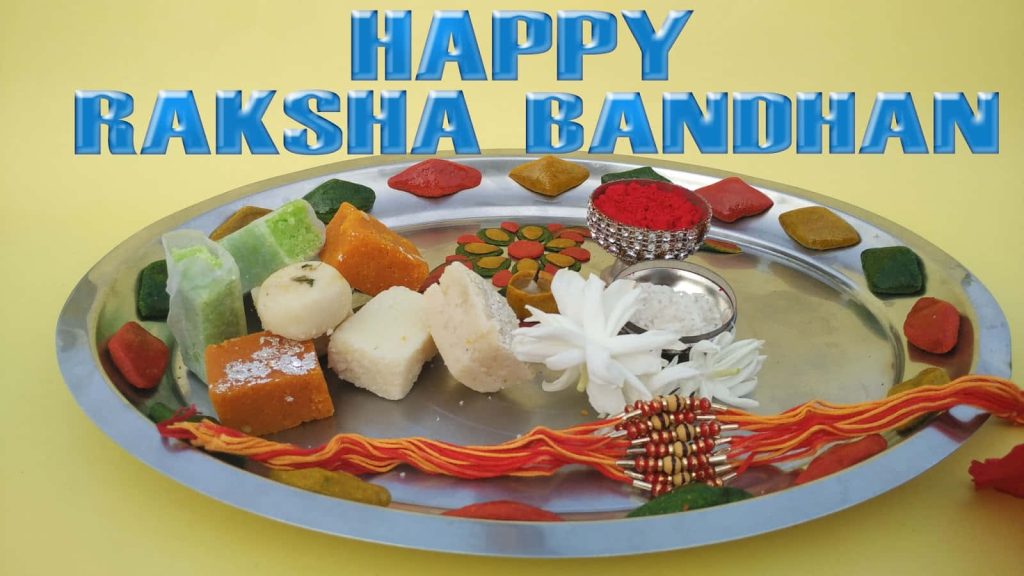 Raksha Bandhan thali with rakhi sweets flowers kumkum on yellow background festive wallpaper