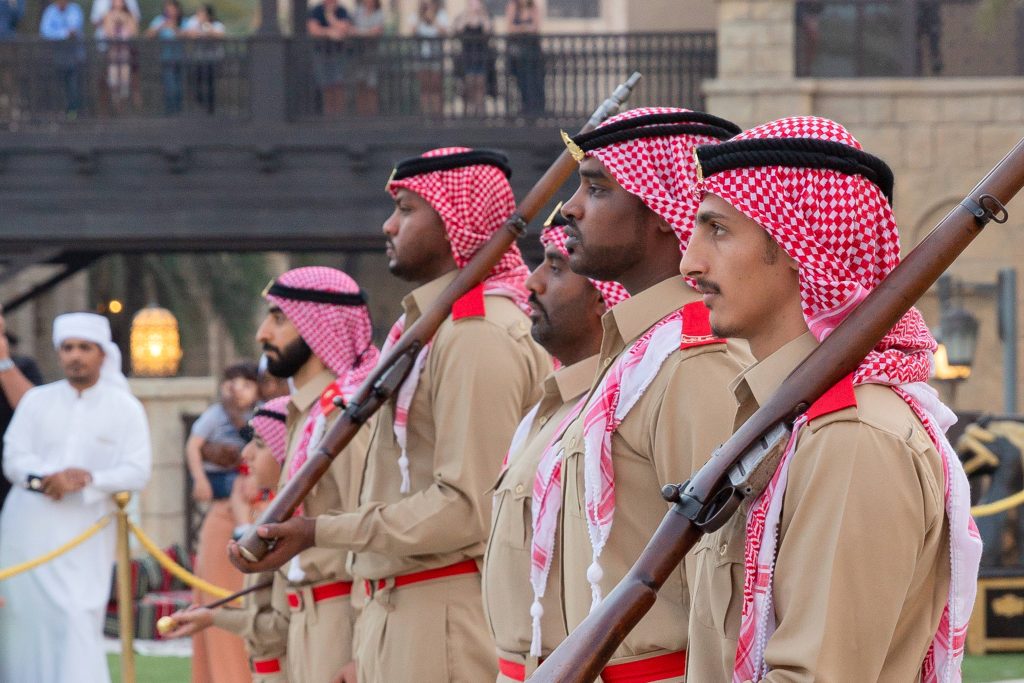 Ramadan Elite Guards in tan uniforms with red ghutras holding vintage rifles in formation Wallpaper