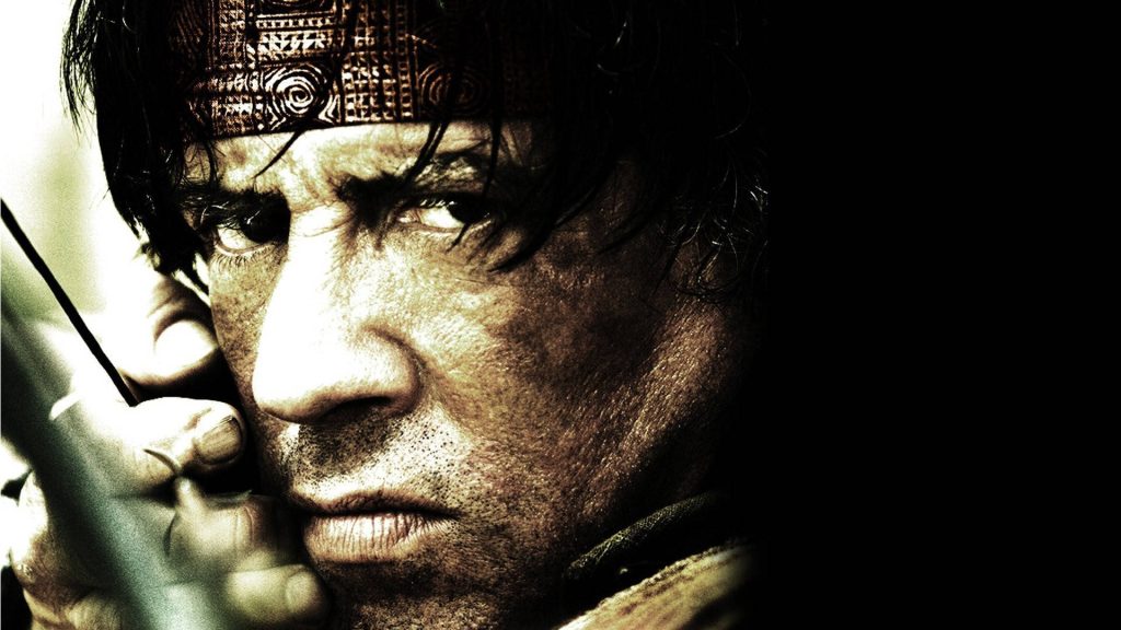 Close-up of Sylvester Stallone as John Rambo gripping bow in intense high-contrast action wallpaper