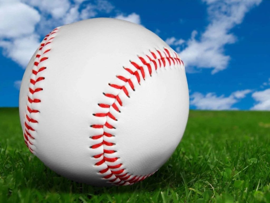 Close-up of white baseball with red stitching on green grass under bright blue sky wallpaper background