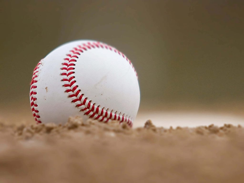Close-up of a white baseball with red stitching on dusty pitcher's mound in soft natural light Wallpaper