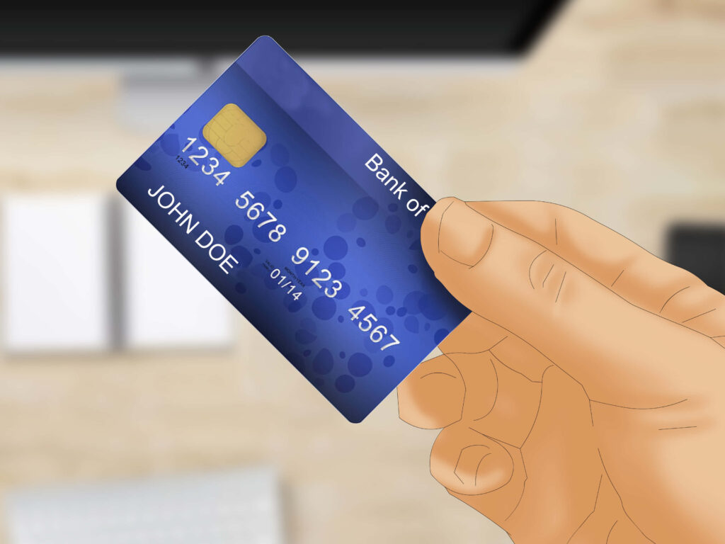 Hand holding blue credit card with name John Doe blurred computer screen online shopping desk Wallpaper
