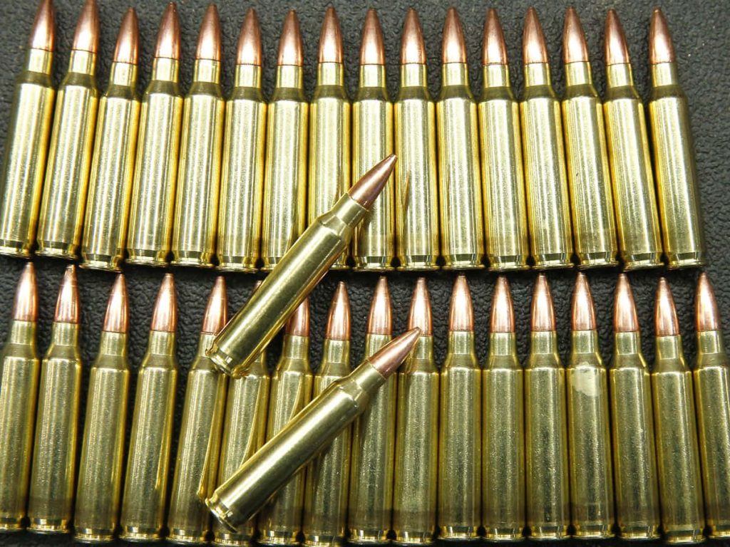 Rows of brass 556 NATO rifle cartridges with two polished copper jacketed bullets on dark background Wallpaper
