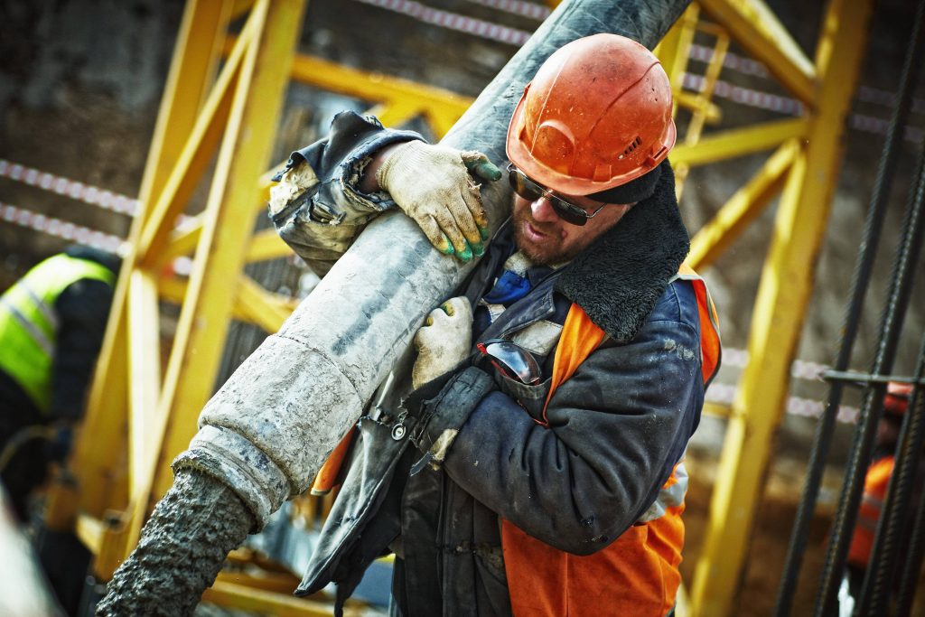 Construction worker in safety gear operating concrete pump hose on yellow scaffolding site Wallpaper