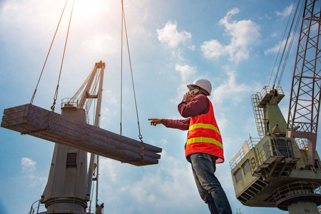 Construction worker in high-visibility vest directing crane lift on active sunny site wallpaper background