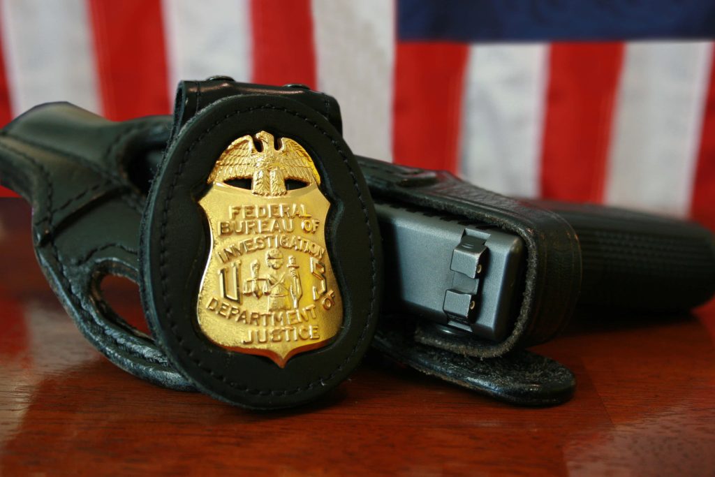 Close-up of metallic FBI badge in black leather holster with blurred American flag background Wallpaper