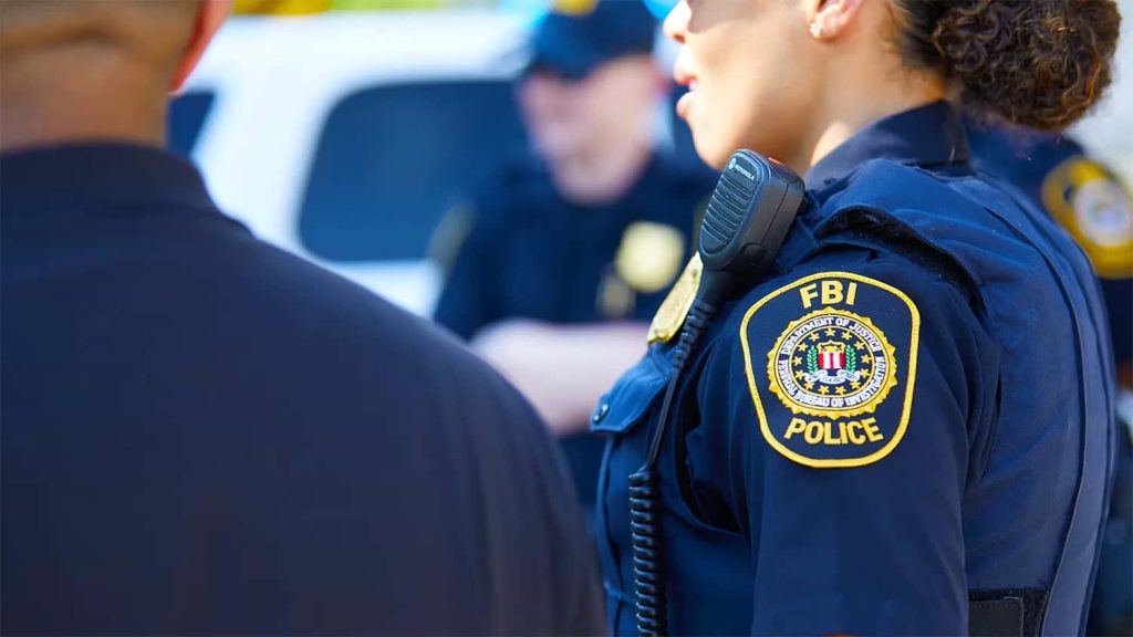Realistic FBI Police officer outdoors showing official shoulder patch with colleague in background Wallpaper