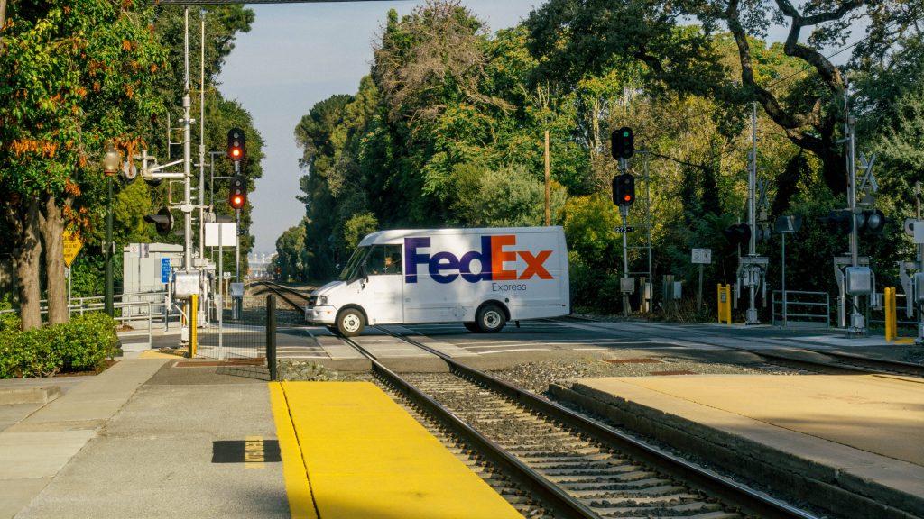 FedEx Express van crossing railway tracks surrounded by greenery and urban transit signals wallpaper