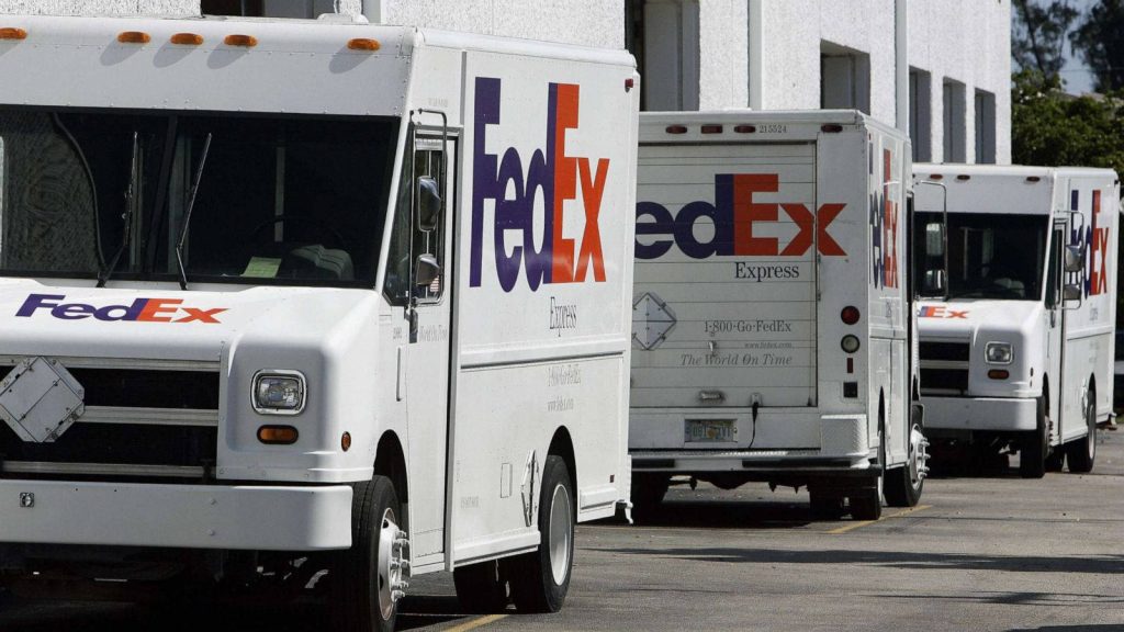 Fleet of white FedEx Express delivery trucks parked in a row on paved lot in bright daylight Wallpaper