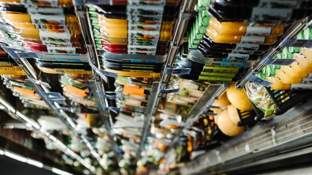 Refrigerated grocery aisle with packaged foods sausages and cheeses under bright lights wallpaper