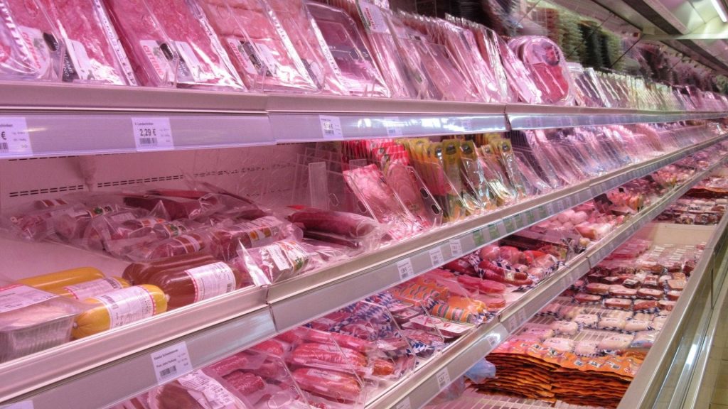 Well-stocked supermarket refrigerator with packaged meats salami sausages in bright retail lighting Wallpaper