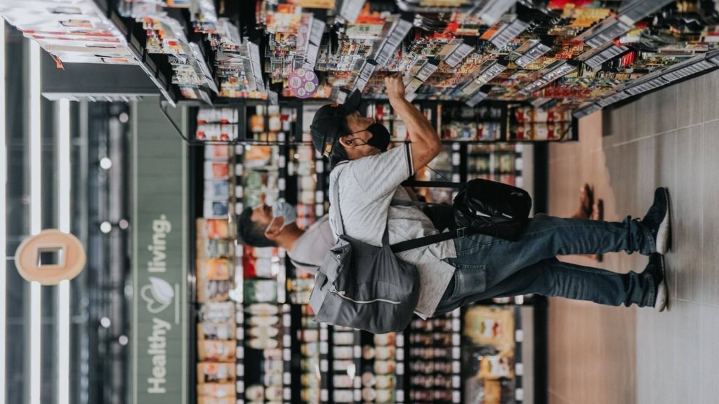 Man in mask with backpack browsing groceries under healthy living sign in modern supermarket aisle Wallpaper