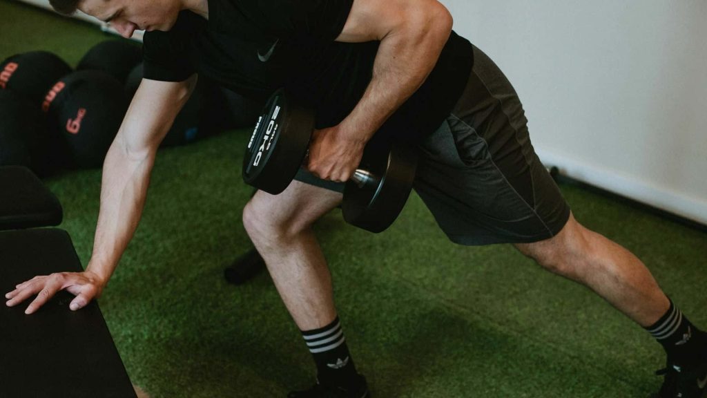 Athlete doing unilateral dumbbell row with 20kg weight on green turf for gym motivation Wallpaper