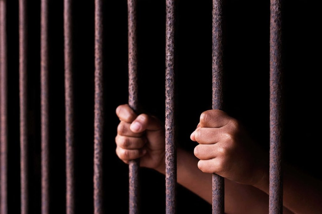 Hands gripping rusted prison bars in dark background symbolizing isolation and confinement Wallpaper