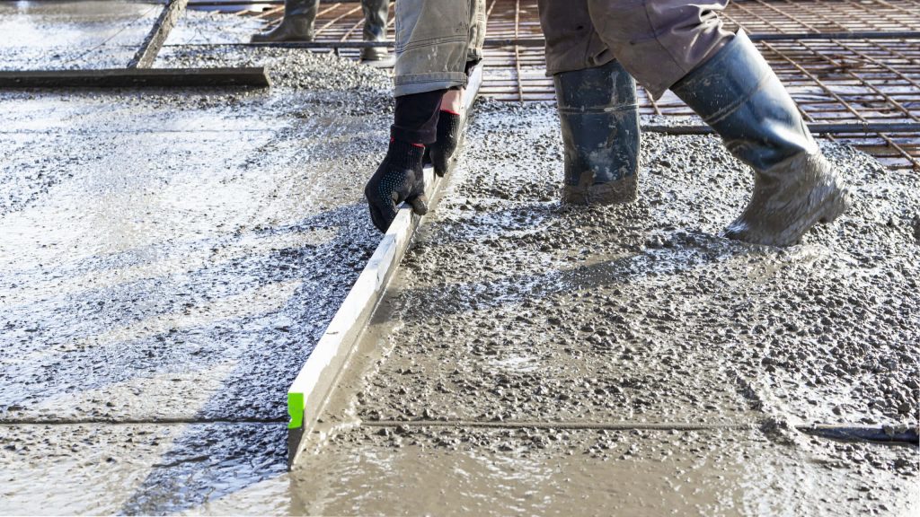 Workers leveling fresh wet concrete with metal screed and rubber boots on textured floor Wallpaper