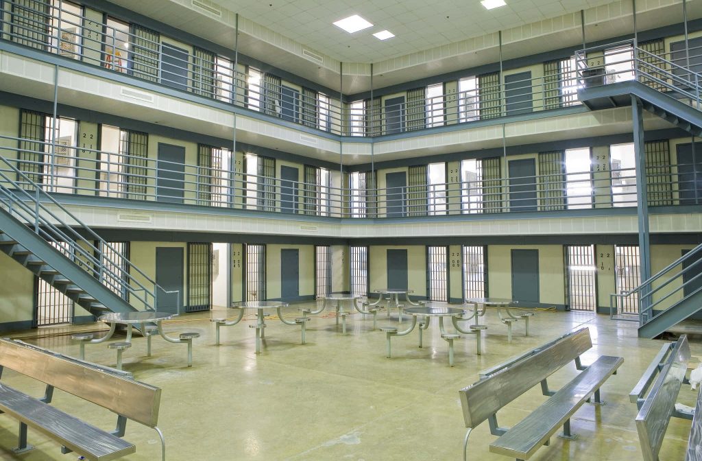 Modern prison interior with multi-tiered cell block metal staircases and stainless steel tables Wallpaper