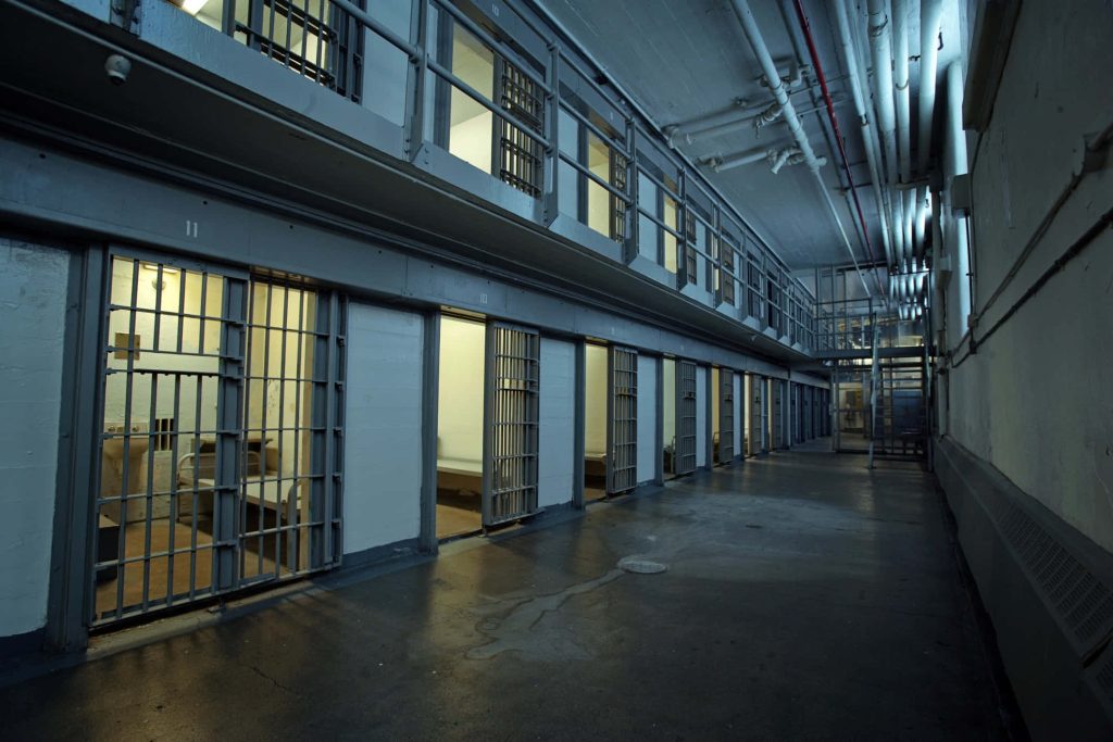 Multi-tiered prison cell block with metal bars cold lighting and exposed industrial pipes interior Wallpaper