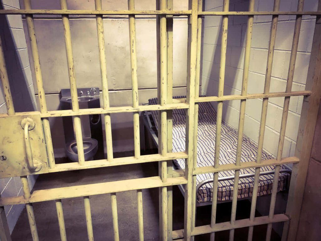 Prison cell interior with iron bars stainless steel toilet striped mattress bleak lighting wallpaper