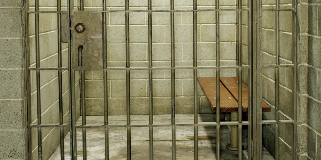 Realistic jail cell wallpaper with steel bars concrete walls wooden bench somber lighting