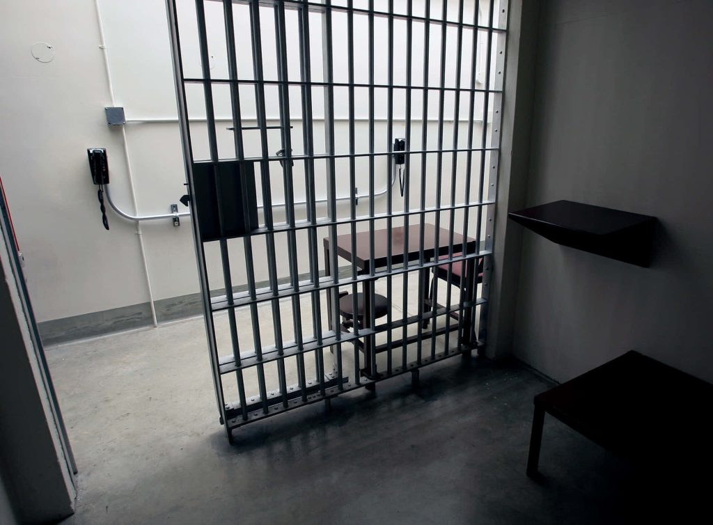 Realistic prison visitation room wallpaper with metal bars table and wall phones somber atmosphere