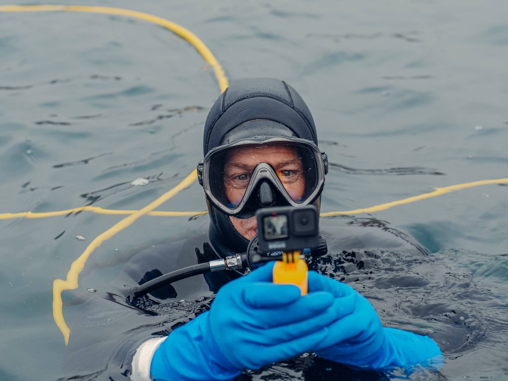 Scuba diver surfacing in open water with GoPro on yellow grip wearing black wetsuit and blue gloves Wallpaper