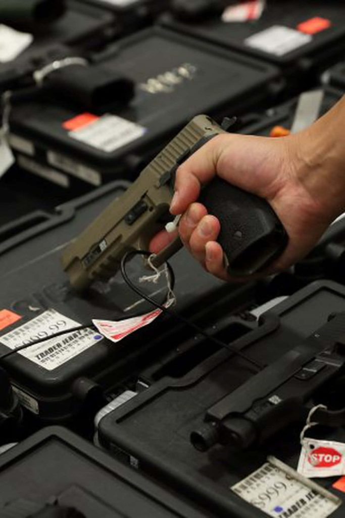 Hand holding tan semi-automatic pistol in gun shop with black cases and price tags wallpaper