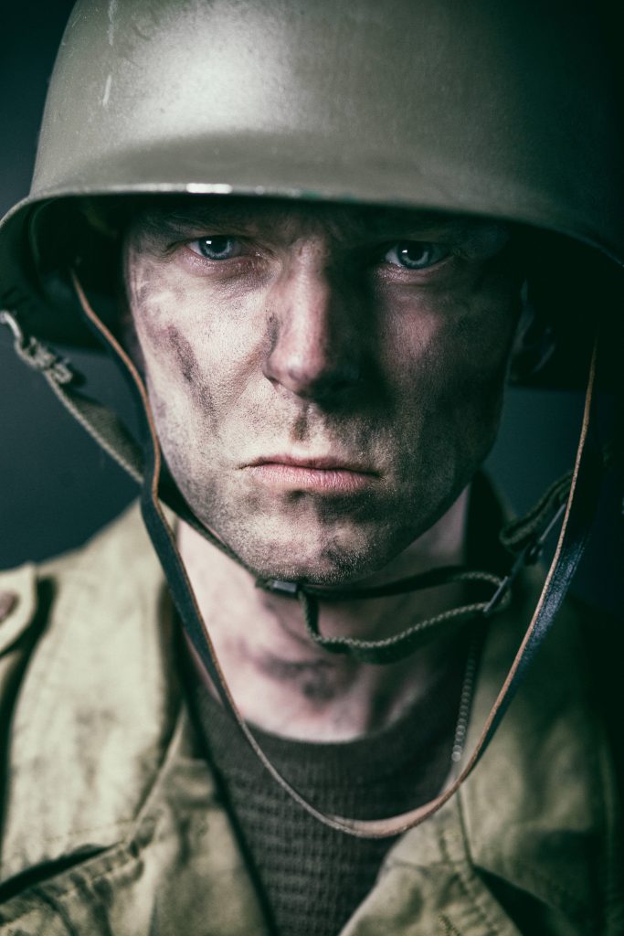 Close-up of a battle-worn soldier with olive helmet dirt-smudged face intense gaze war wallpaper