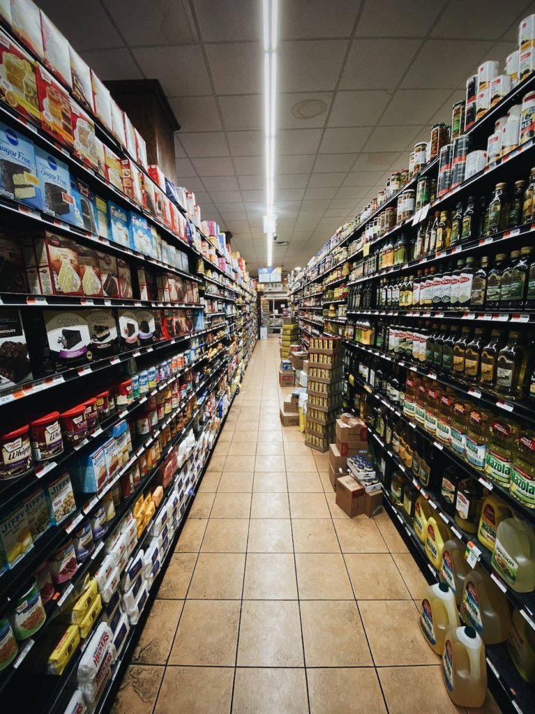 Wide-angle view of messy grocery store aisle with packed shelves oils baking mixes scattered boxes Wallpaper
