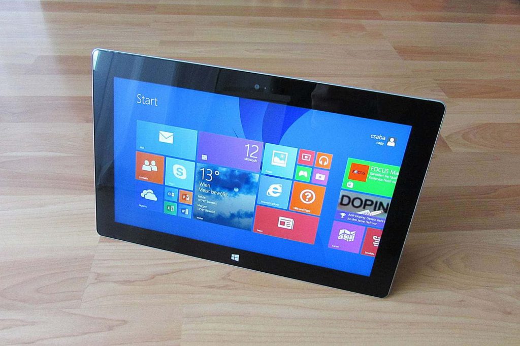 Tablet showing vibrant colorful Windows 8 Start screen with Metro UI on light wooden table Wallpaper