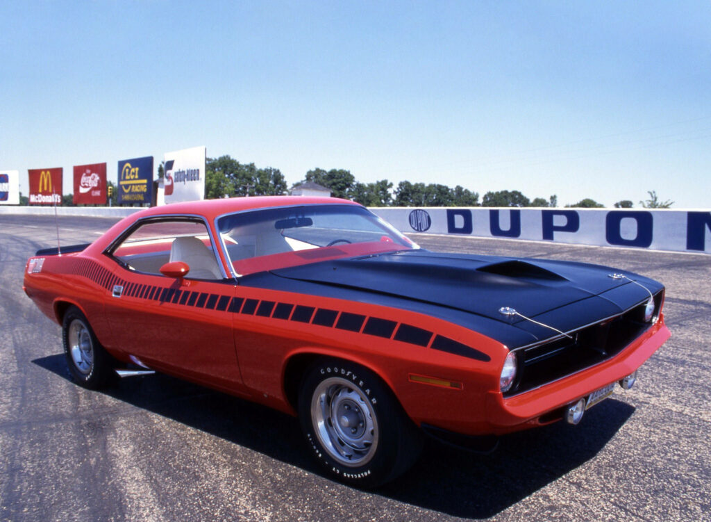 Red 1970 Plymouth Barracuda muscle car with black accents parked on racetrack under blue sky Wallpaper
