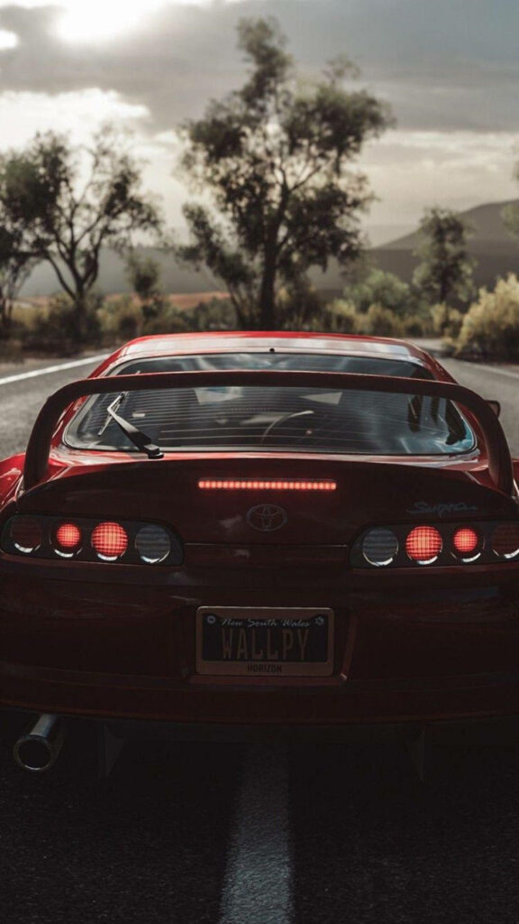 Rear view of red 1996 Toyota Supra Mk4 with iconic taillights on scenic open road background Wallpaper