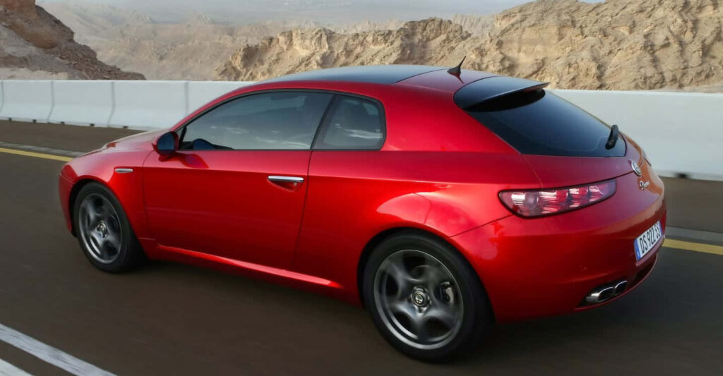 Red Alfa Romeo Brera sporty car driving on scenic mountain road with rugged natural backdrop wallpaper