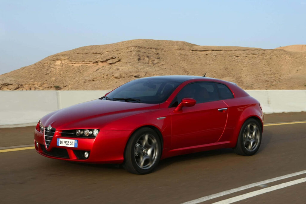 Red Alfa Romeo Brera speeding on desert road with rocky landscape dynamic car wallpaper background