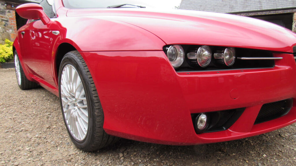 Red Alfa Romeo Brera parked on gravel driveway with sleek design and countryside background Wallpaper